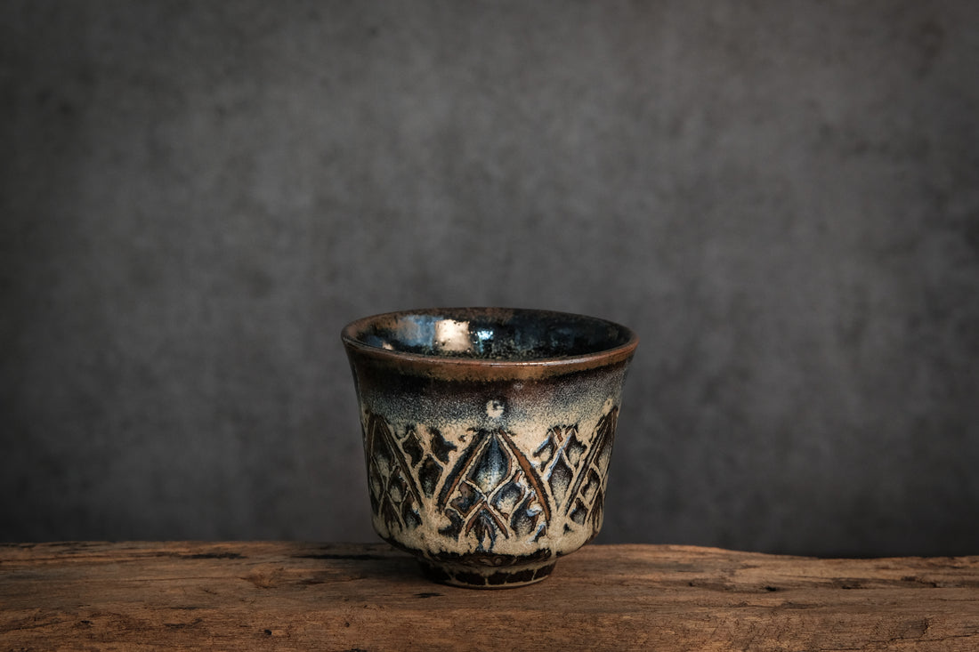 unique tea cup, with carved patterns. the glaze creates a beautiful interplay of deep blue and light brown tones.