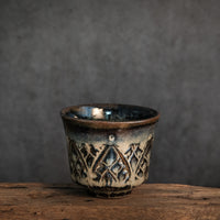 unique tea cup, with carved patterns. the glaze creates a beautiful interplay of deep blue and light brown tones.