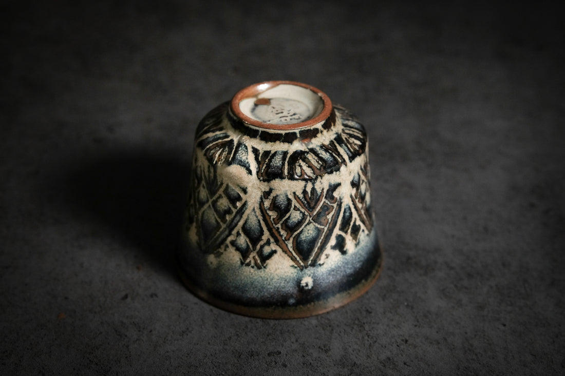 unique tea cup, with carved patterns. the glaze creates a beautiful interplay of deep blue and light brown tones.