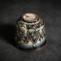 unique tea cup, with carved patterns. the glaze creates a beautiful interplay of deep blue and light brown tones.