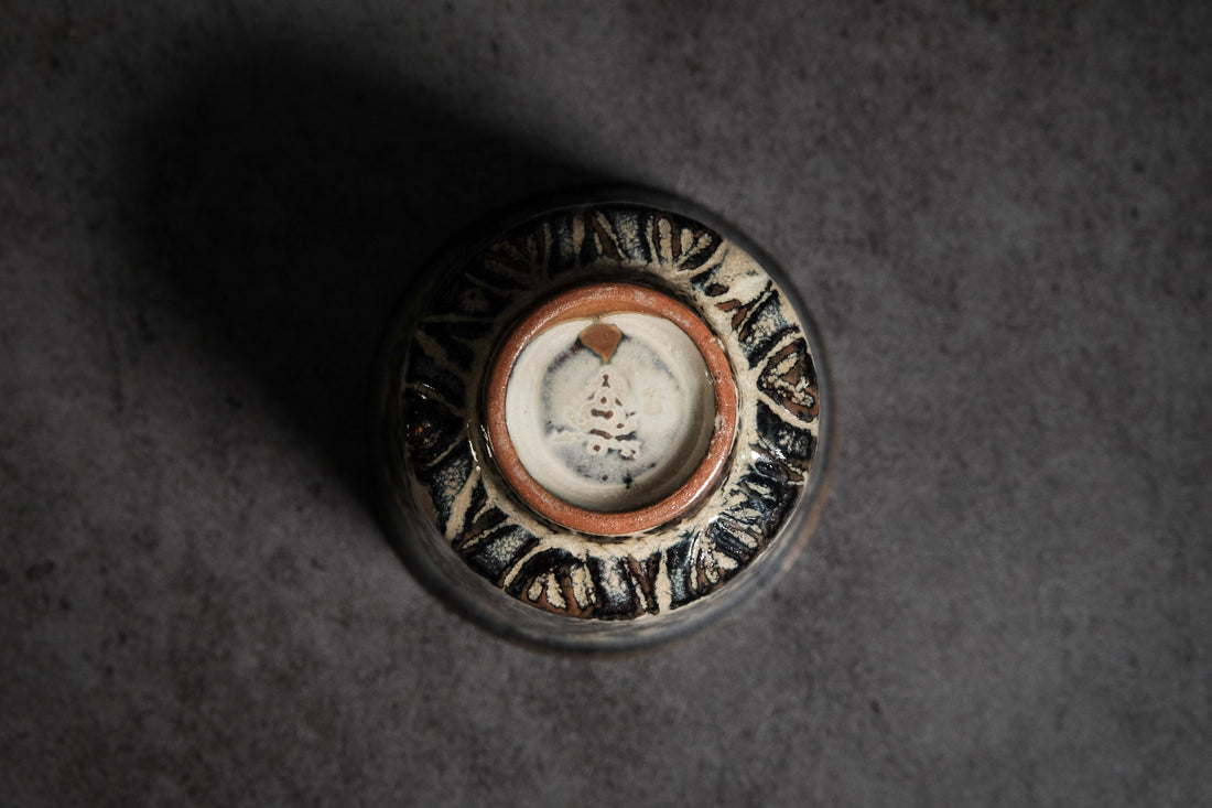 unique tea cup, with carved patterns. the glaze creates a beautiful interplay of deep blue and light brown tones.